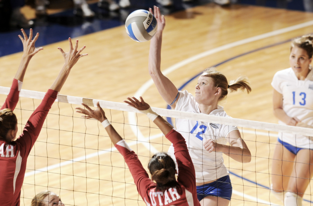 Volleyball player hitting ball over net while opposing team defends.
